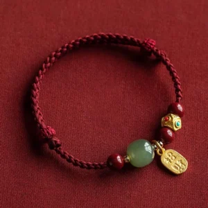 Hetian jade prosperity bracelet flat lay with cyan jade bead, cinnabar beads, and gold lucky charm pendant on red background