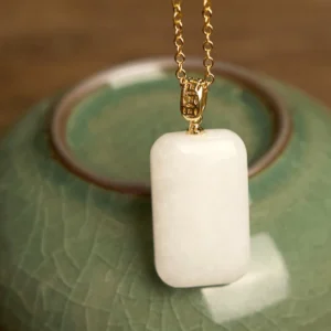 Hetian jade rectangular pendant necklace with gold metal chain, polished white jade close-up on ceramic teapot backdrop