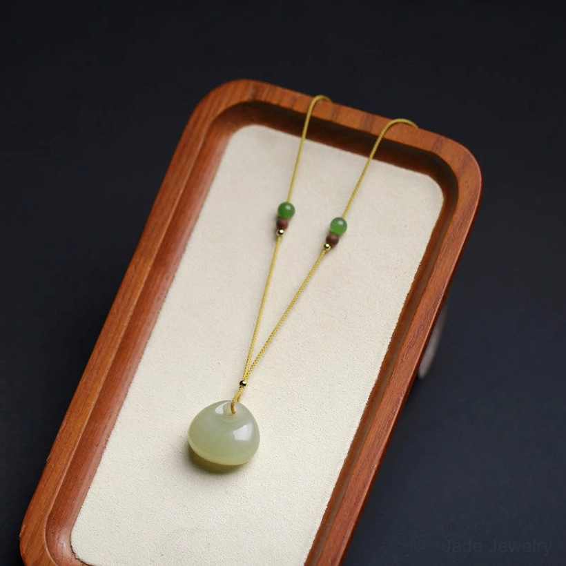 Hetian jade good fortune pendant necklace symmetric display, well-finished light green jade charm on wooden tray with soft lighting
