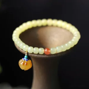 Hetian jade pumpkin prosperity bracelet with amber carved pendant and red agate beads on ceramic holder, close-up view