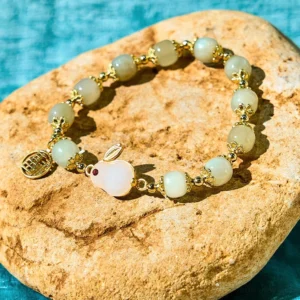 Hetian jade rabbit prosperity bracelet with Fu character charm, 8mm light green jade beads and gold-plated accents on textured stone background