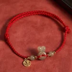 Hetian jade rabbit head peace buckle fu character red string bracelet with gold charms on red background