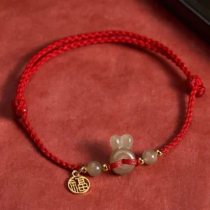 Hetian jade rabbit head peace buckle fu character red string bracelet with gold charms on red background