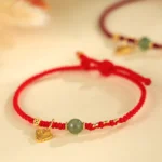 Red string Hetian jade bracelet with sterling silver heart charm and copper coin, top-down close-up on neutral background