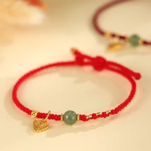 Red string Hetian jade bracelet with sterling silver heart charm and copper coin, top-down close-up on neutral background