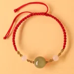 Hetian jade braided string bracelet with red cord and gold metal accents flat lay top view on warm background