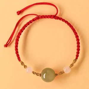 Hetian jade braided string bracelet with red cord and gold metal accents flat lay top view on warm background