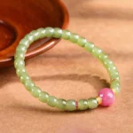 Hetian jade and rhodonite prosperity bracelet with gold accents on wooden surface, overhead view showcasing green jade beads and pink rhodonite focal bead
