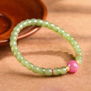 Hetian jade and rhodonite prosperity bracelet with gold accents on wooden surface, overhead view showcasing green jade beads and pink rhodonite focal bead