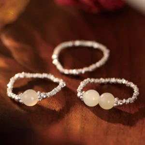 Flat lay of adjustable jade beaded rings on dark wooden surface - single and double jade bead variants