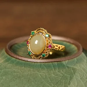 Vintage jade inlaid luck ring side view, showing gold hollow filigree frame with light beige jade oval center and decorative gem accents