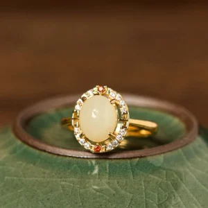 Natural Hetian jade adjustable ring with cubic zirconia halo and gold-plated copper band, front flat lay view on celadon ceramic