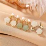 Assorted Hetian jade rose pearl earrings collection in gold-plated silver with white and green jade on warm fabric background