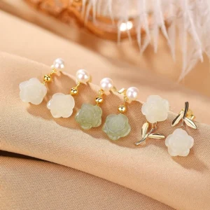 Assorted Hetian jade rose pearl earrings collection in gold-plated silver with white and green jade on warm fabric background