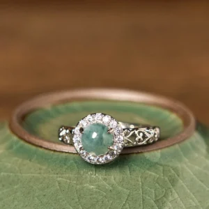 Hetian jade ruyi prosperity ring flat lay on green ceramic vessel, top-down view of filigree design