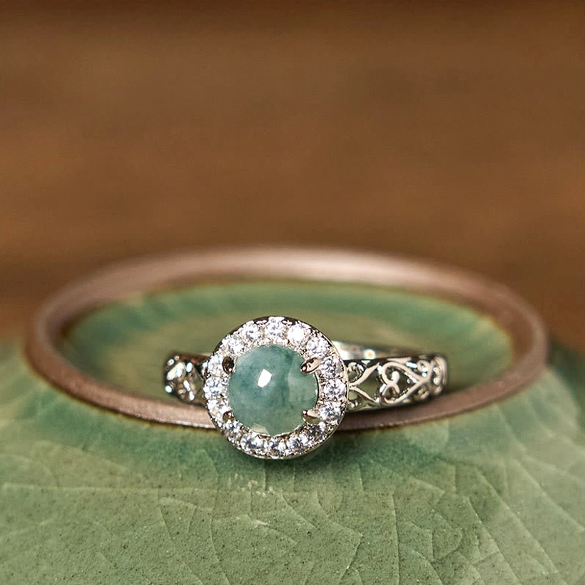 Hetian jade ruyi prosperity ring flat lay on green ceramic vessel, top-down view of filigree design