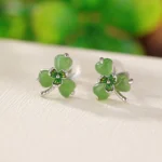 Hetian jade shamrock stud earrings in 925 sterling silver, top-down flat lay view showing delicate clover design with green jade stones