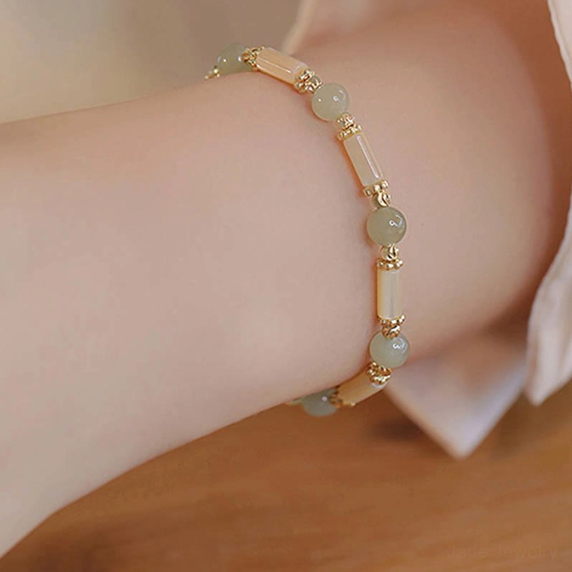 Single-layer hetian jade beaded bracelet with shell tube beads and gold spacers, side view on wooden table styling