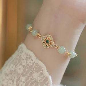 Hetian jade square charm bracelet worn on wrist with lace sleeve, pale green jade beads with ornate gold hollow square pendant