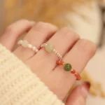 Three stackable hetian jade and sterling silver beaded elastic rings in light green jade, red agate, and pearl styles worn on hands