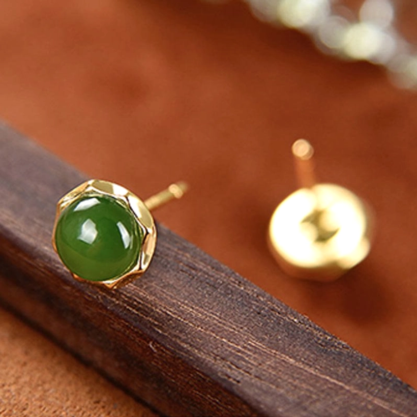Close-up of polished green jade stud earring with scalloped hexagonal gold bezel setting on wooden display board
