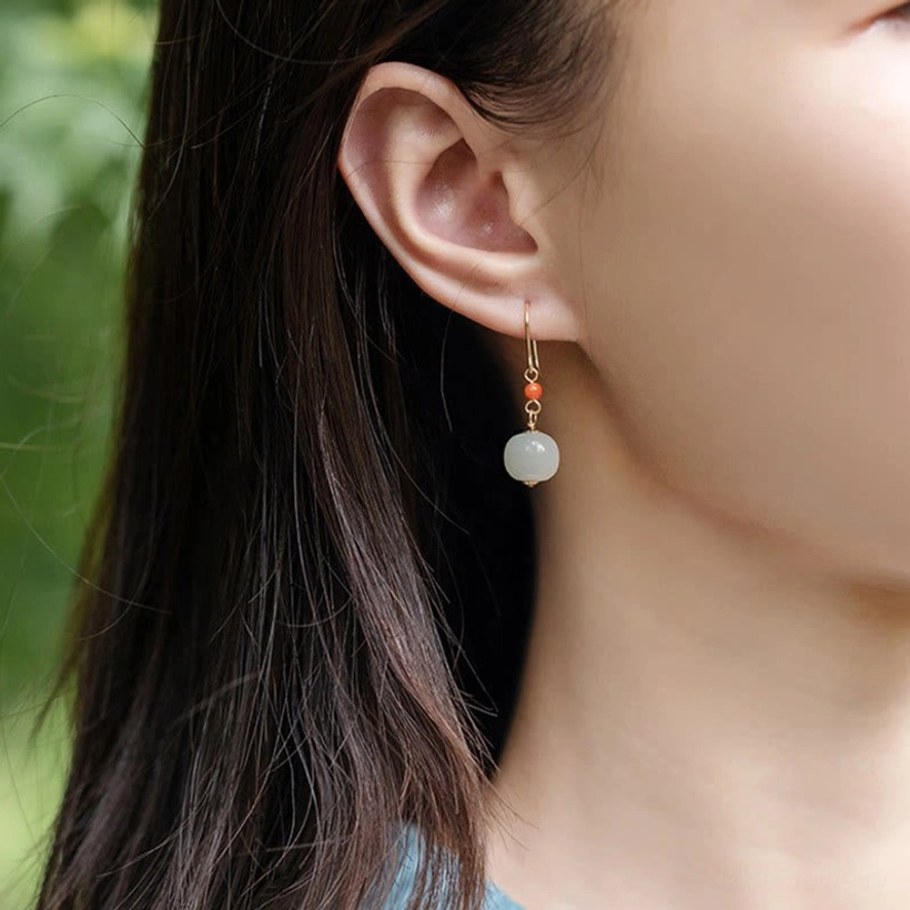Close-up side view of woman wearing pale white hetian jade drop earrings with red agate showing ear and neck area