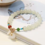 Hetian white jade money bag blessing bracelet with gold-plated hardware and multicolor accent beads on patterned background