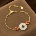 Gold-plated peace buckle Hetian white jade bracelet displayed on brown velvet cushion, showing white jade donut pendant with red decorative beads and thin gold chain
