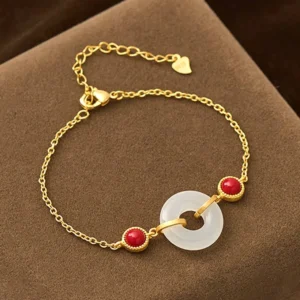Gold-plated peace buckle Hetian white jade bracelet displayed on brown velvet cushion, showing white jade donut pendant with red decorative beads and thin gold chain