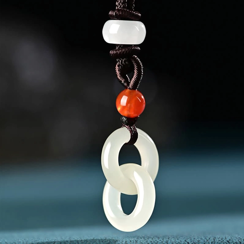 Close-up front view of white jade double peace buckle pendant with braided cord and red agate beads