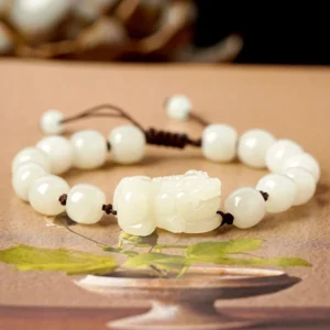 Hetian white jade Pixiu wealth bracelet with round jade beads and brown braided cord on wooden display