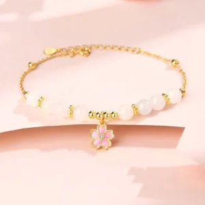 Hetian white jade cherry blossom protection bracelet with 925 sterling silver chain, flat lay view featuring pink enamel sakura pendant and white jade beads on pink studio backdrop