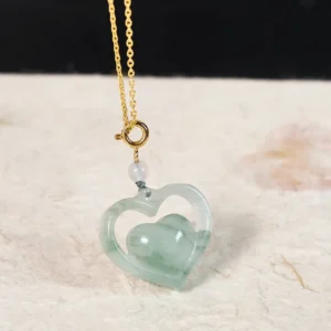 Hollow heart jade pendant necklace side view on beige fabric with gold chain and jade bead accent detail