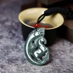 Horse-dragon jade pendant carved in intricate hollow relief, photographed at an oblique angle on a traditional Chinese tea table with black rope and red decorative bead