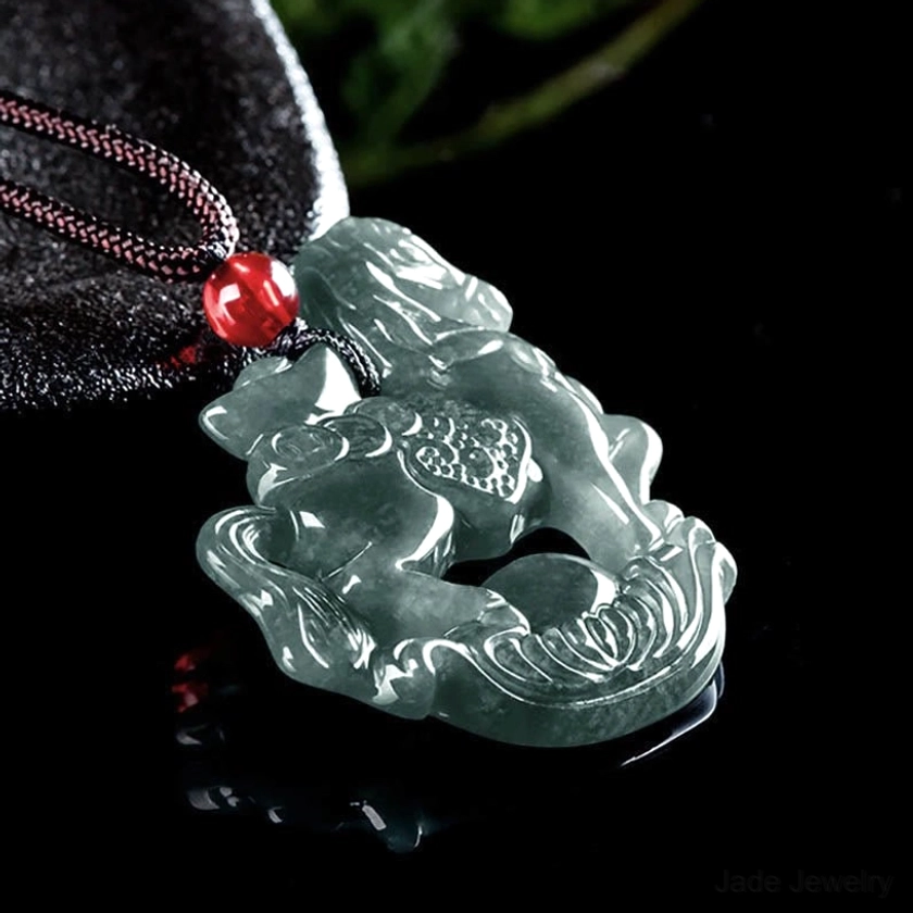 Side profile view of horse jade pendant necklace on dark velvet background showing carved pendant design with hanging loop and red accent bead on dark cord