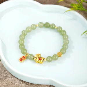 Year of the horse jade bracelet overhead view displaying matte green jade beads with gold charms and red fortune tag on ceramic plate