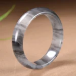 Ink wash golden silk jade bangle bracelet with black and white marbling, 15mm width, polished finish on brown textured table
