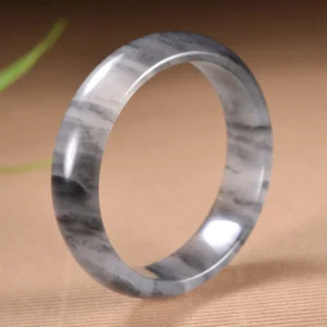Ink wash golden silk jade bangle bracelet with black and white marbling, 15mm width, polished finish on brown textured table