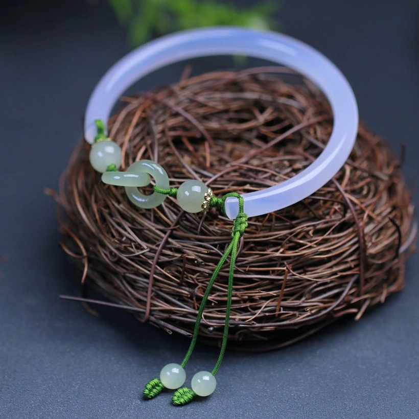 Hetian jade interlocking bracelet bangle with light blue band and green cord jade accents, three-quarter view on wicker nest background