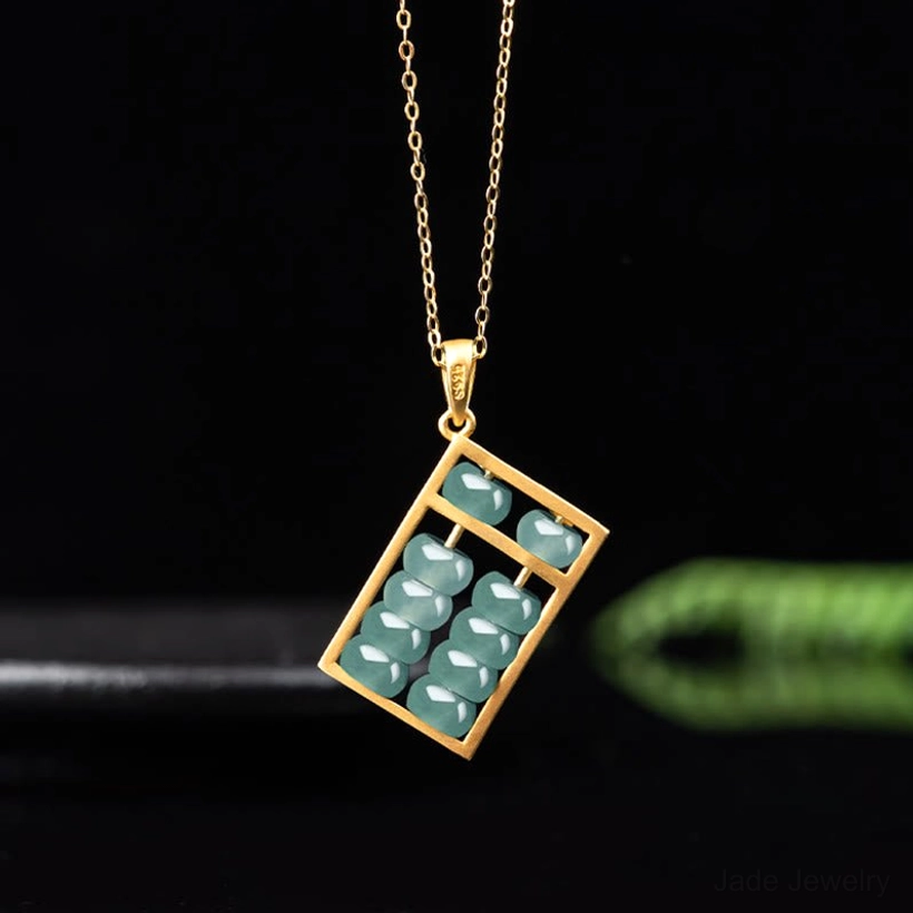 Gold-tone jade abacus necklace pendant displayed at angle with thin delicate chain on dark green background