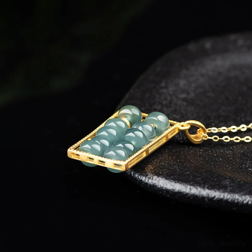 Gold-tone jade abacus pendant with movable jade beads shown overhead on black stone base with thin chain