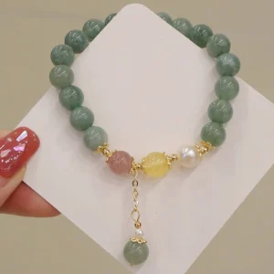 Close-up angled view of jade prosperity bracelet held by hand with red nail polish, displaying dangling jade pendant and mixed gemstone beads on product card