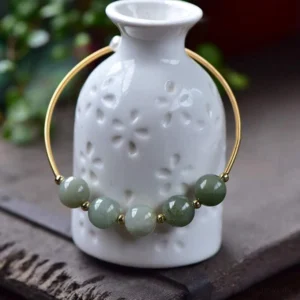 Three-quarter view of green jade beaded cuff bracelet with 14K gold hoop and spacer beads, styled on white ceramic vase