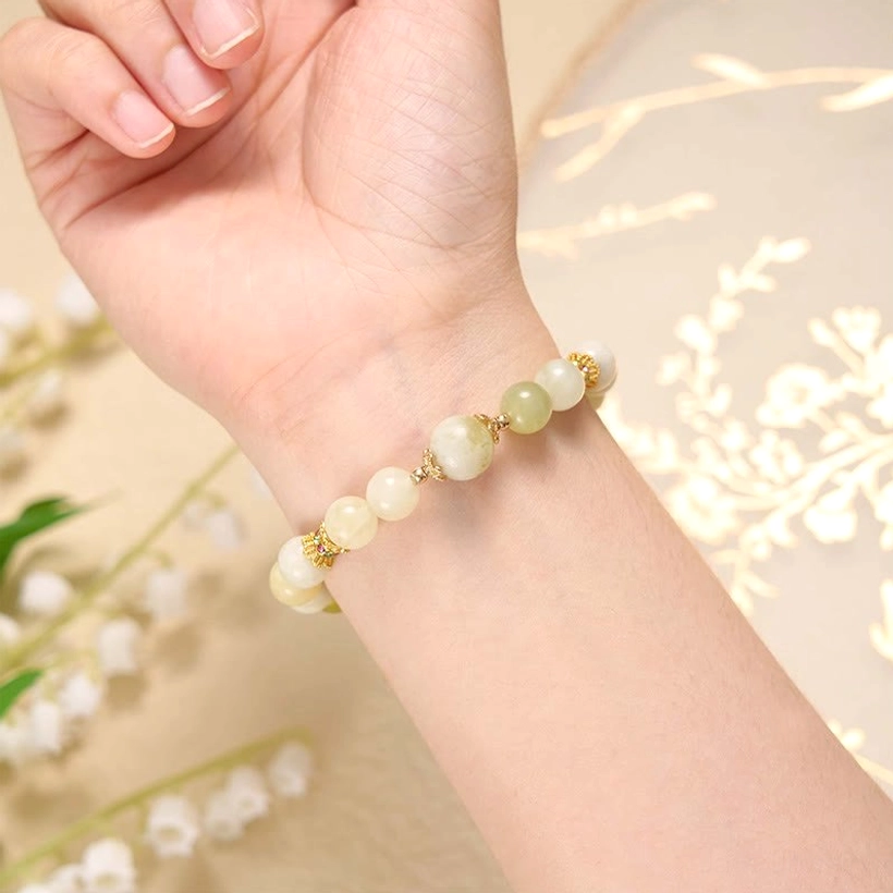 Dainty green jade prosperity bracelet worn on wrist with floral background