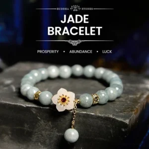 Light green jade flower bracelet with white floral charm and red gem accent, displayed on dark stone with dangling jade bead detail