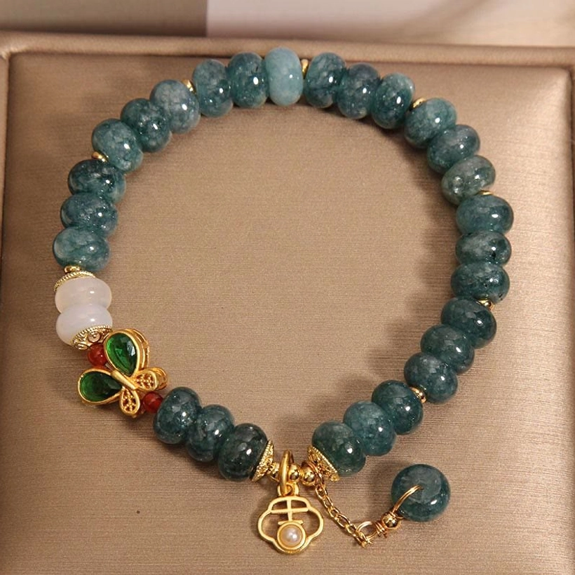 Single strand jade beaded bracelet with white agate bead and green enamel butterfly charm on open jewelry tray