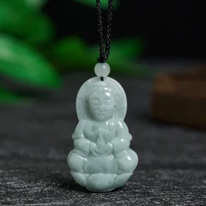 Pale green jade Avalokitesvara Guanyin pendant necklace with detailed carving, front view displayed on dark stone with botanical background