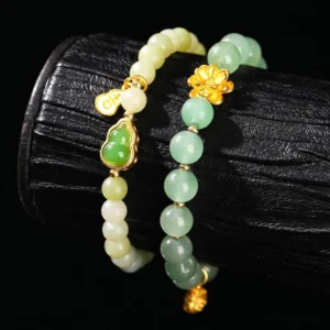 Stacked jade and green aventurine lucky bracelets with gold floral and gourd accents displayed on black wooden cylinder