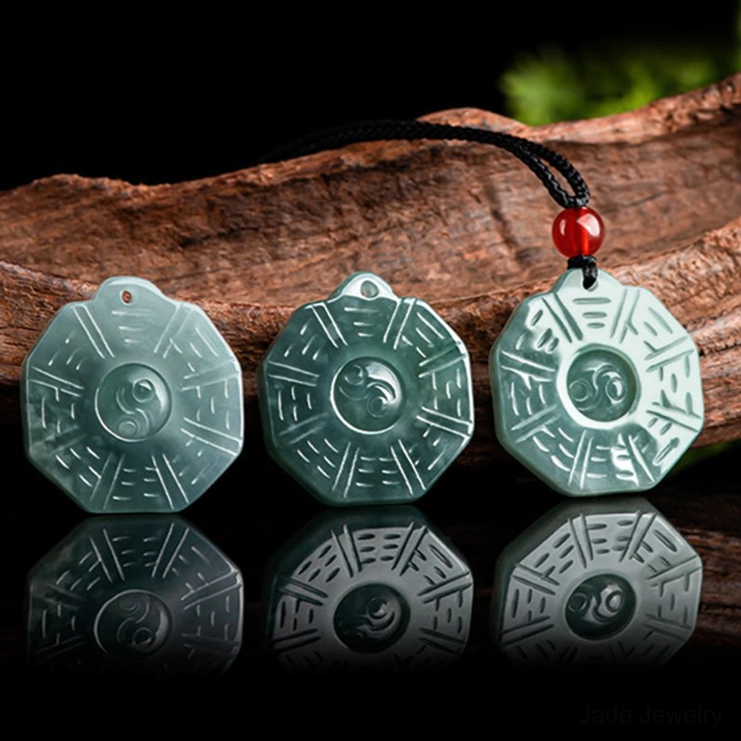 Set of three matching natural jade Bagua Yin Yang pendants displayed overhead with mirror reflections on dark background