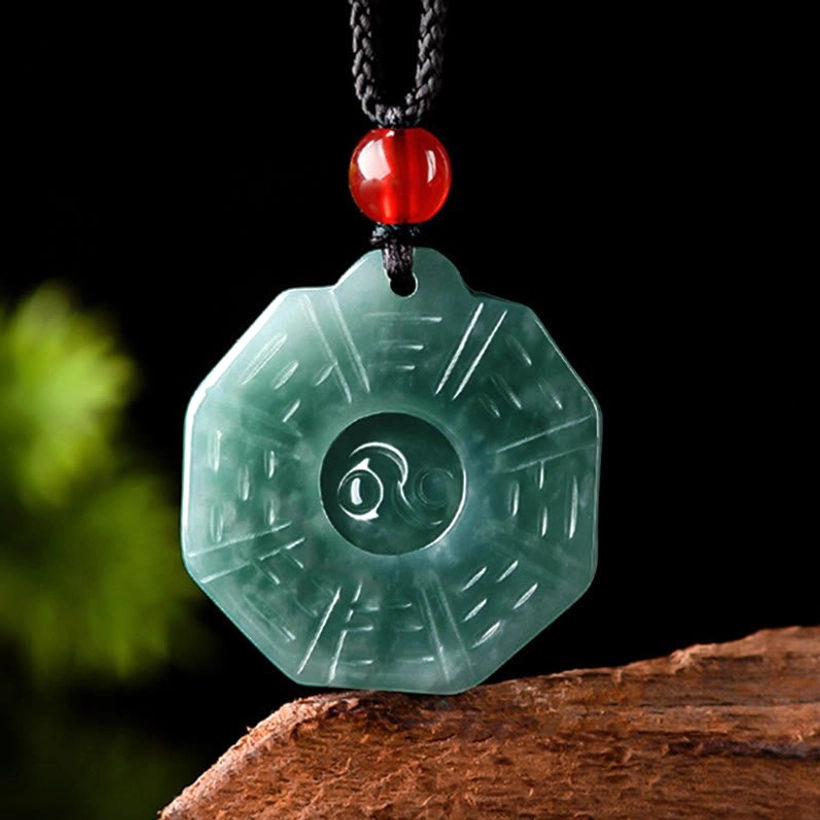 Close-up flat lay of translucent dark green jade Bagua necklace showing intricate carved trigram designs on wooden surface